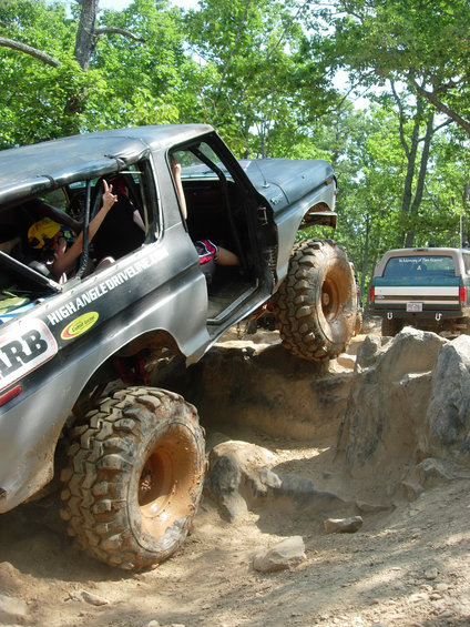 1996 Ford Bronco - Modified off-road vehicles tackle a challenging rocky trail with trees in the background.