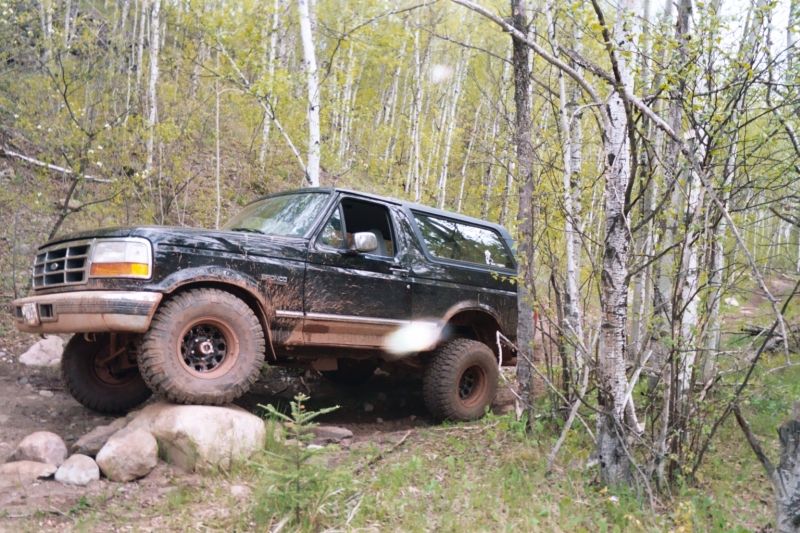 Black Ford Bronco with lifted suspension and off-road tires navigating a rocky trail, front-left tire on a large boulder
