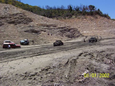 1985 Ford Bronco - Several off-road vehicles are stuck in thick mud on a dry, rocky hillside.
