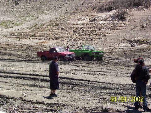 1985 Ford Bronco - Two trucks are stuck in the mud, with people observing the scene.