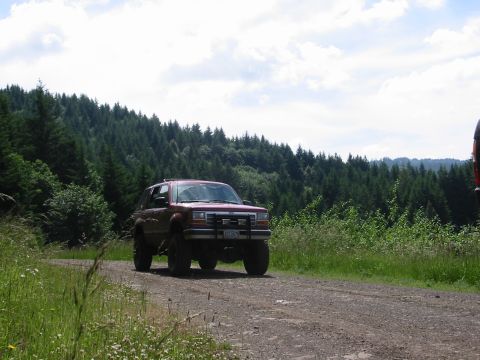 1991 Ford Explorer - A red 1991 Ford Explorer drives on a gravel road through a wooded area.