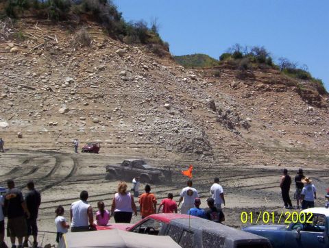 1985 Ford Bronco - A muddy pickup truck navigates a dry lake bed, with several vehicles and spectators present.