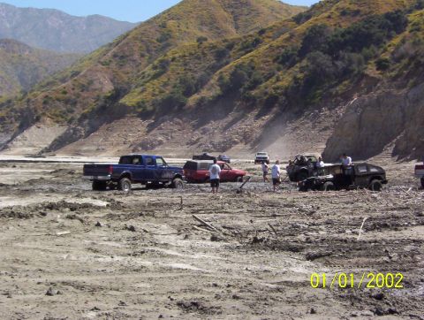 1985 Ford Bronco - A group of off-road vehicles are seen in a muddy, dry riverbed with mountains in the background. The photo is dated January 1, 2002.