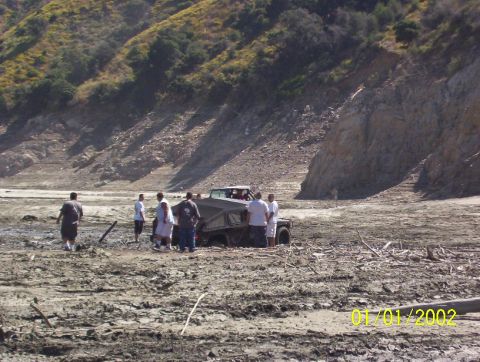 1985 Ford Bronco - A group of people stand around a vehicle in a desolate, dry landscape. The date 01/01/2002 is visible in the lower right corner.