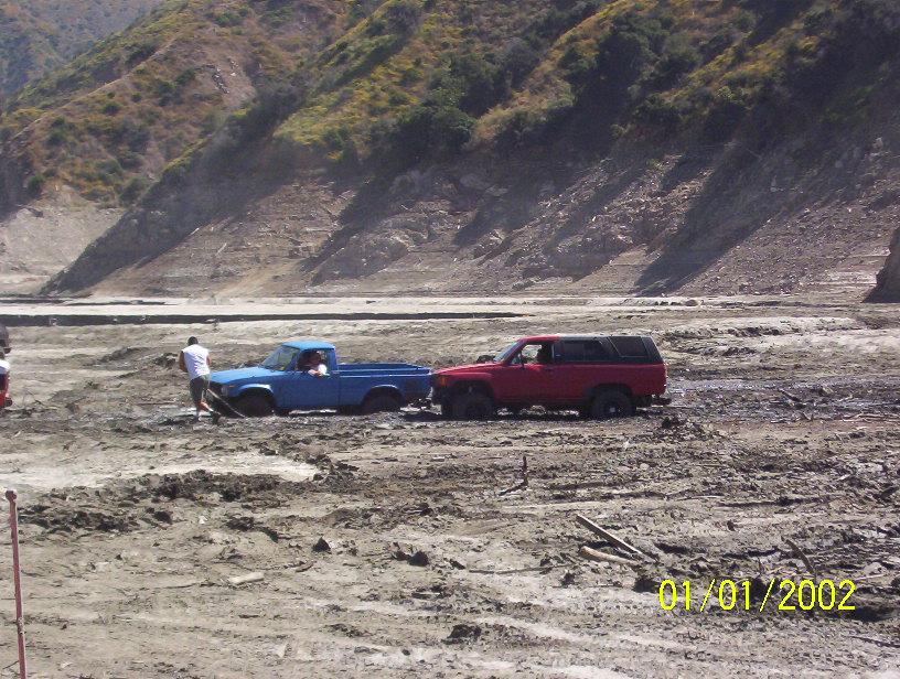 Red SUV and blue pickup truck stuck in mud with people nearby