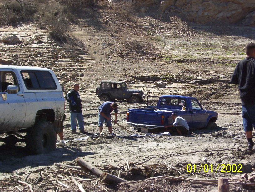 Several off-road vehicles stuck in mud with people trying to free them