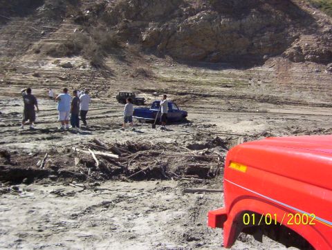 1985 Ford Bronco - Several people stand around vehicles in a muddy, outdoor area with a large rocky hill in the background.