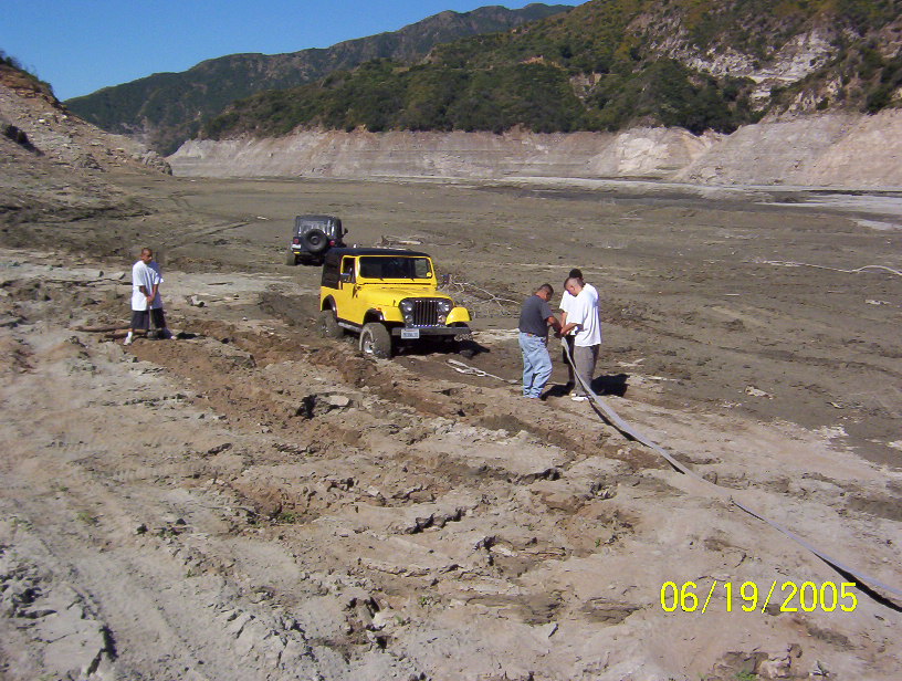 Yellow Jeep CJ stuck in mud on a dry lakebed while three men rig a recovery line