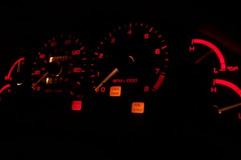 1997 Ford Probe - Illuminated car dashboard gauges display speed, RPM, fuel level, and warning lights in the dark.