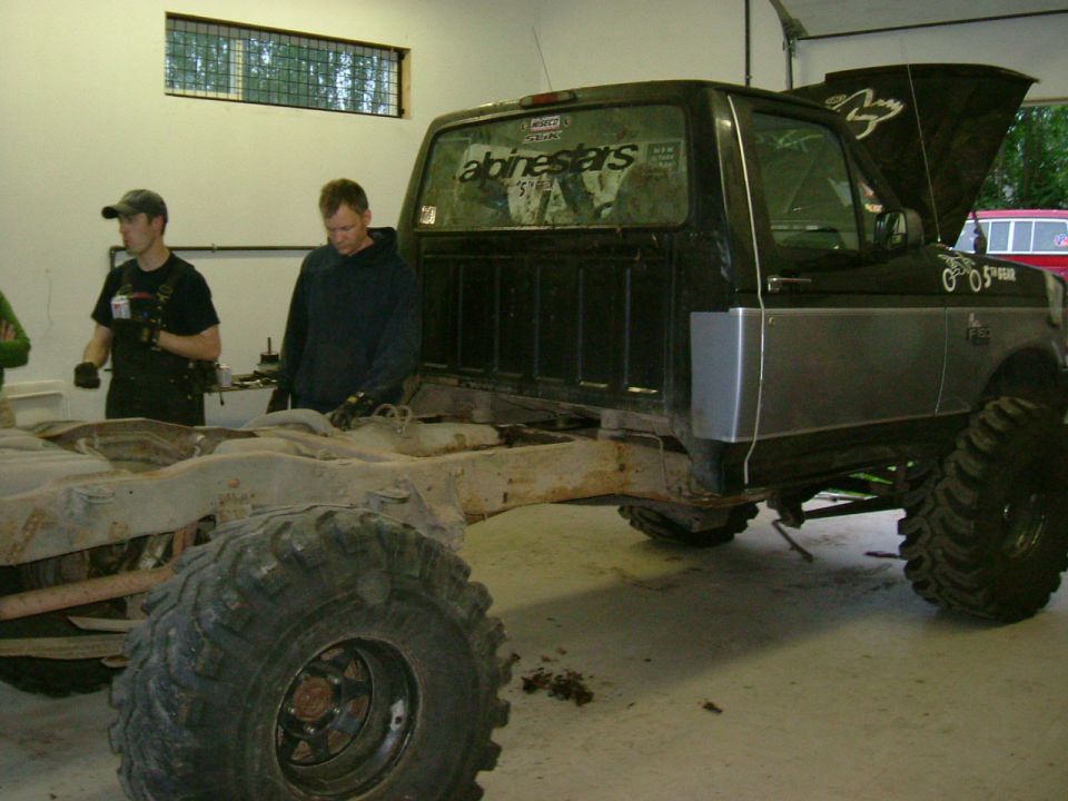 Black pickup truck chassis with large tires and two men working on it