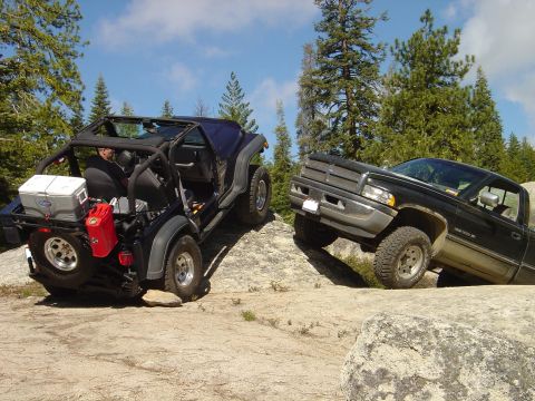 1989 Ford Bronco - Two modified off-road vehicles are seen climbing a steep, rocky incline on a sunny day.