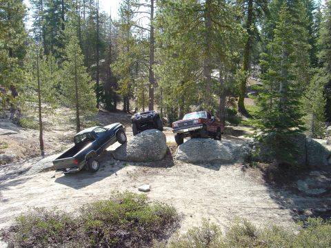 1989 Ford Bronco - Three off-road vehicles traverse a challenging rocky path through a wooded area.