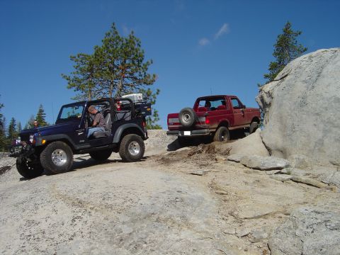 1989 Ford Bronco - A red 1989 Ford Bronco navigates a challenging rocky trail, with a blue Jeep following behind.