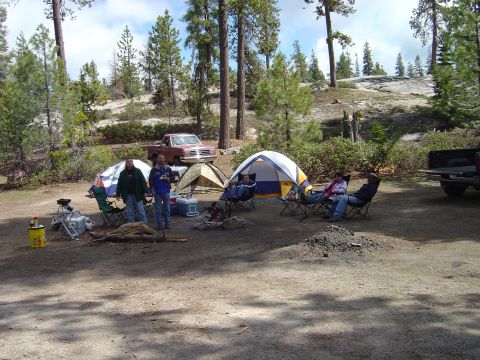 1989 Ford Bronco - A red pickup truck is parked at a campsite with tents and people enjoying the outdoors.