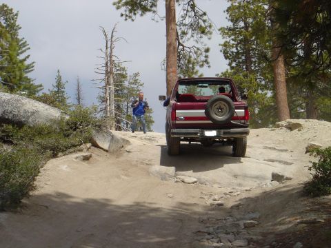 1989 Ford Bronco - A red SUV navigates a rocky trail surrounded by trees.