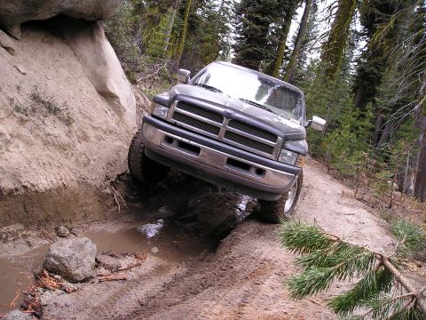 1989 Ford Bronco - Dodge Ram pickup truck struggles on a steep, muddy, off-road trail.
