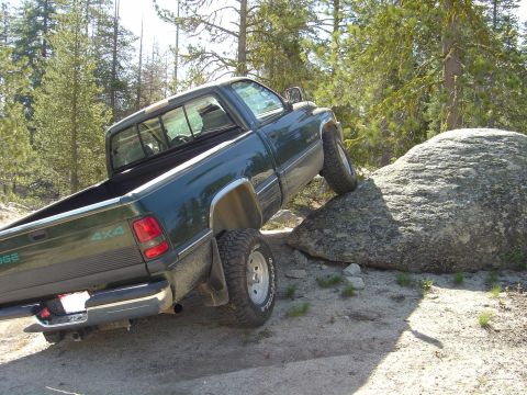 1989 Ford Bronco - A green Dodge pickup truck navigates an off-road obstacle, with its right front tire placed on a large boulder.