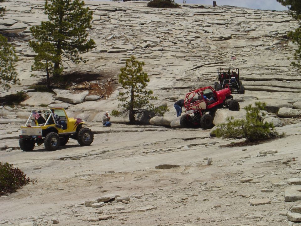 Yellow off-road vehicle on rocky terrain with red and black vehicles behind