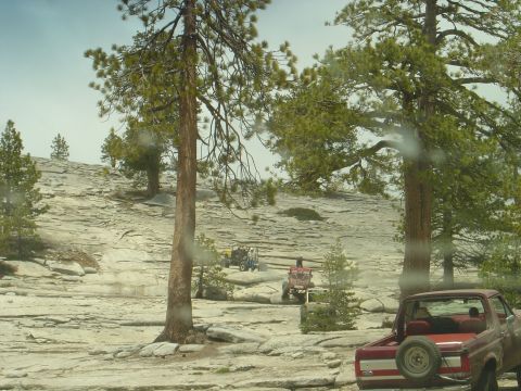 1989 Ford Bronco - A red pickup truck is parked on rocky terrain, with other off-road vehicles visible in the distance.