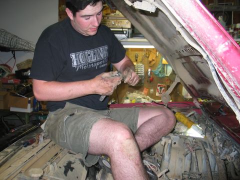 1995 Ford Bronco - A mechanic works on the engine of a red vehicle in a garage.