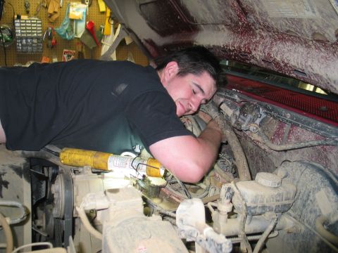 1995 Ford Bronco - A mechanic is deep in the engine bay, working on a complex system of hoses and wires.
