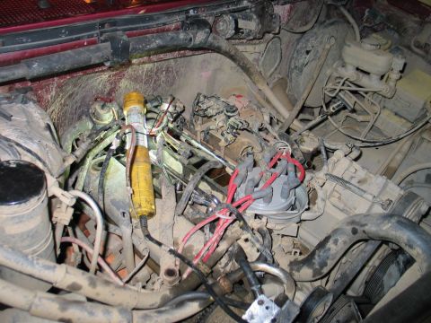 1995 Ford Bronco - Close-up view of a dusty engine bay, showing the distributor cap, spark plug wires, and a work light illuminating the area.