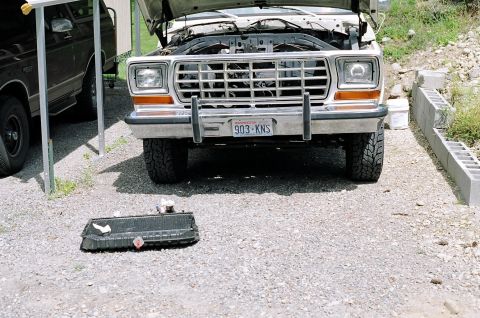1979 Ford Bronco - Front view of a 1979 Ford Bronco with its hood open, and a radiator placed on the gravel in front.