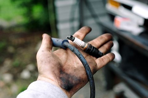 1979 Ford Bronco - A mechanic's hand holds a used spark plug and its corresponding wire, ready for replacement.