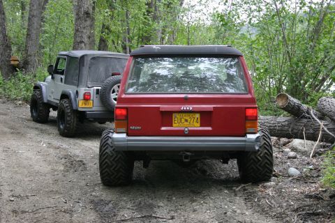 2003 Jeep TJ - Two Jeeps, a red Cherokee and a silver Wrangler, are parked on a dirt trail surrounded by trees.