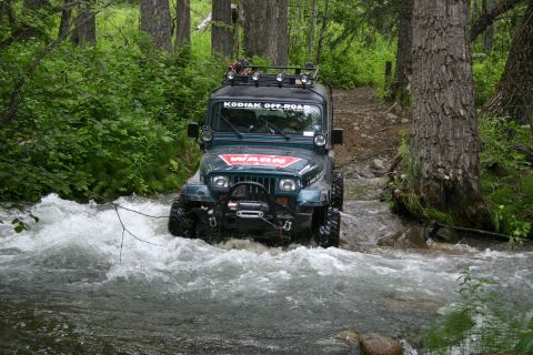 2003 Jeep TJ - A modified Jeep Wrangler navigates through a fast-flowing stream in a wooded area.