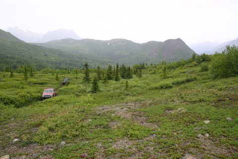 2003 Jeep TJ - Off-road vehicles traverse a scenic, green mountain landscape under an overcast sky.