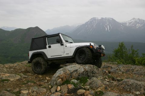 2003 Jeep TJ - A white Jeep Wrangler Rubicon is parked on a rocky outcrop with a mountain range visible in the distance.