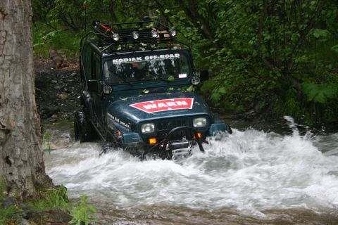 2003 Jeep TJ - A Jeep Wrangler YJ navigates through a shallow, rocky stream surrounded by dense forest foliage.