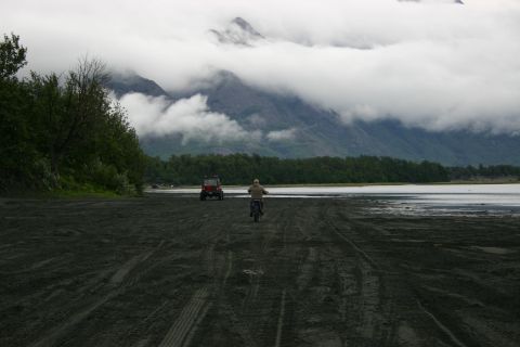2003 Jeep TJ - A red off-road vehicle and a dirt bike are seen on a sandy area near a body of water with mountains in the distance.