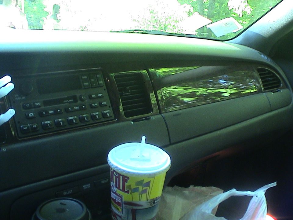 Gray dashboard with woodgrain trim and factory radio; Wendy's cup and plastic bag in foreground