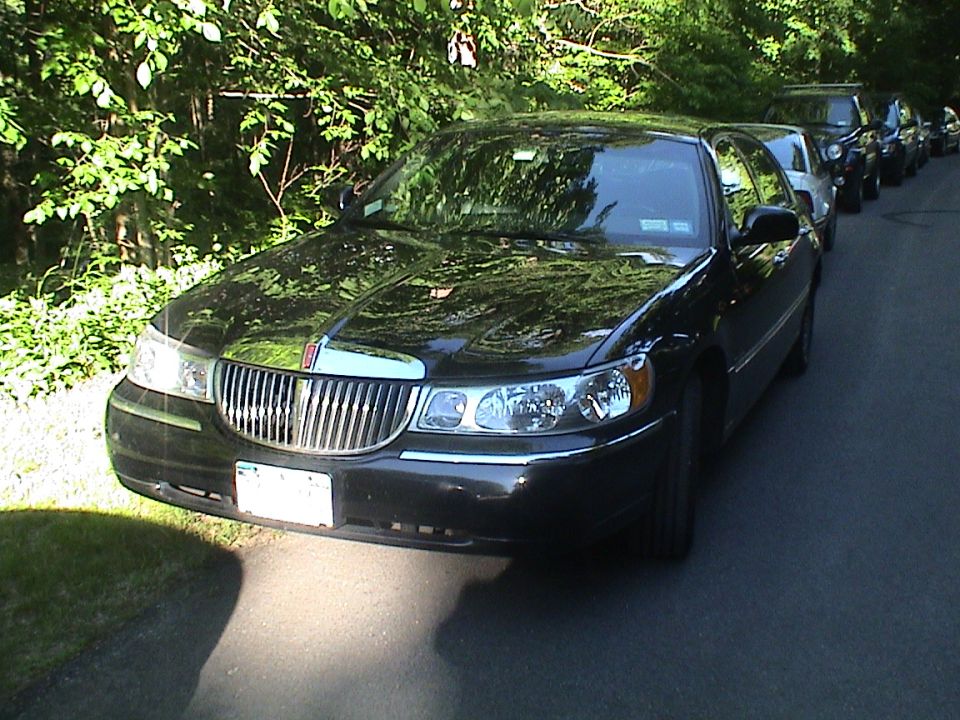 Black Lincoln Town Car sedan parked on a tree-lined road with other cars behind it