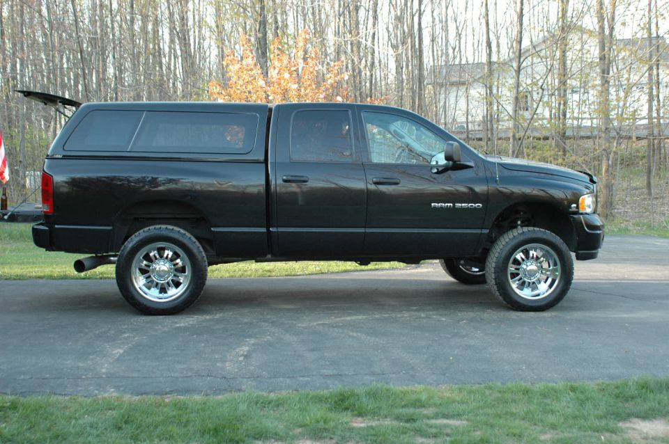 Black Dodge Ram 2500 crew cab pickup with bed topper and lift, side view on driveway