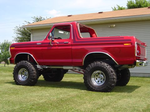 1978 Ford Bronco - Driver-side three-quarter rear-leaning profile of a lifted red full-size Ford Bronco with its removable hardtop off and roll bar exposed, p…