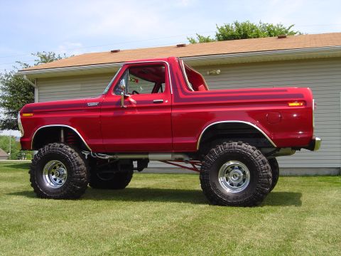 1978 Ford Bronco - Driver-side profile of a lifted red full-size Ford Bronco with the hardtop removed, showing the roll bar, Bronco Ranger XLT fender badge an…