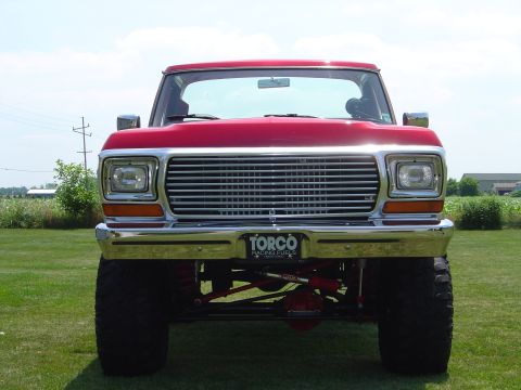 1978 Ford Bronco - This lifted pickup truck features a prominent chrome grille and is parked on a grassy field under a clear sky.