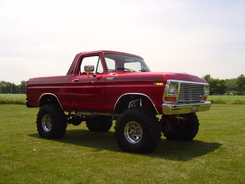 1978 Ford Bronco - Three-quarter front view of a lifted red full-size Ford Bronco with the hardtop removed and roll bar visible, sitting on a grass field with…