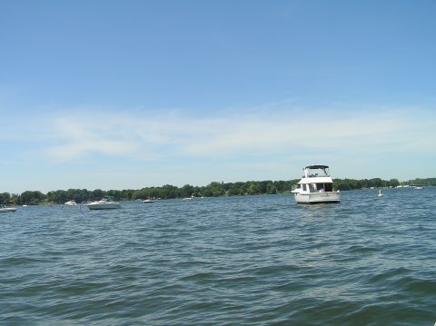 1997 Crownline 266 CCR - A motor yacht cruises on a lake under a clear blue sky with other boats visible.
