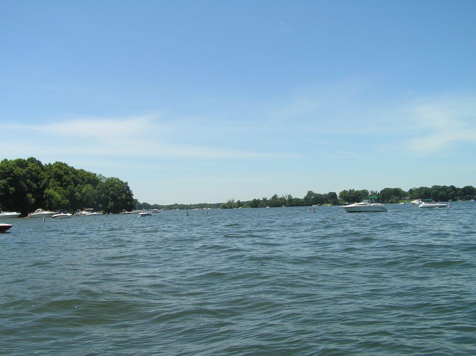 Distant white boats on a calm lake with tree-lined shore and blue sky