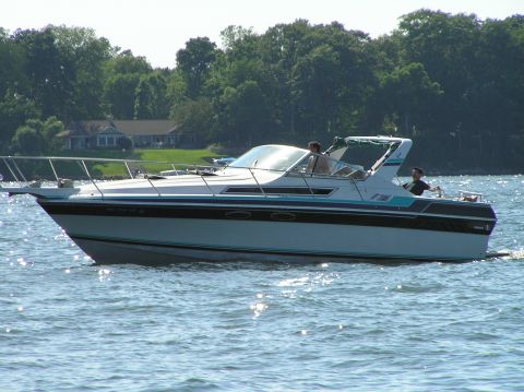1997 Crownline 266 CCR - A motorboat navigates the water on a sunny day, with a residential shoreline visible.