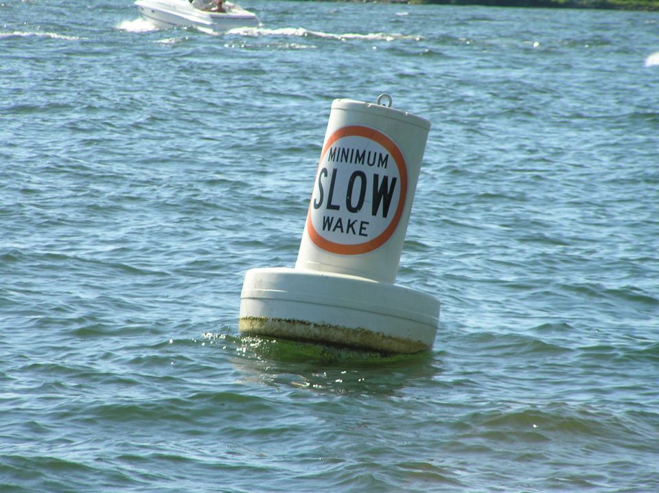 White Minimum Slow Wake buoy on choppy water with a small powerboat in the distance