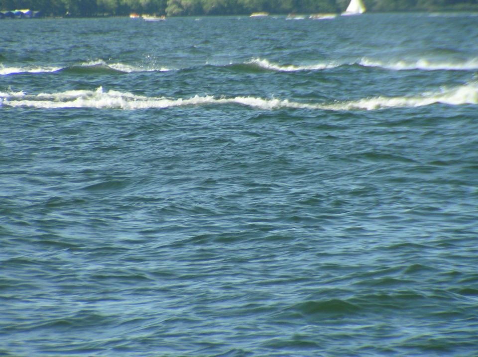Choppy blue-green lake water with waves and a distant shoreline