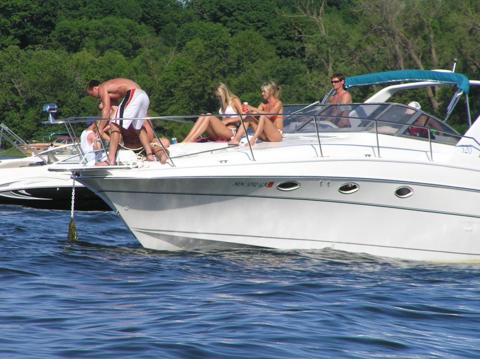 White cabin cruiser boat with people on the bow, anchored on a lake