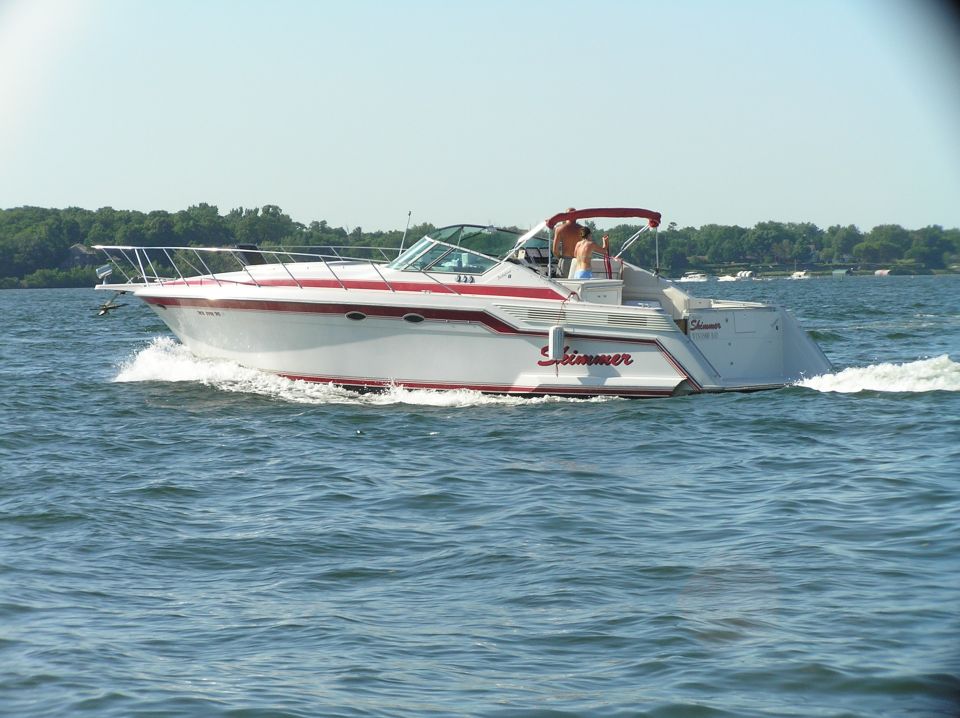 White express cruiser named Skimmer with red stripes underway on a lake, side view