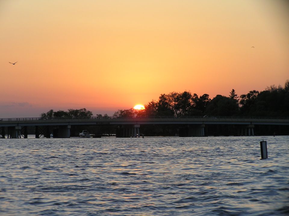 Sunset over water with a bridge silhouette and orange sky