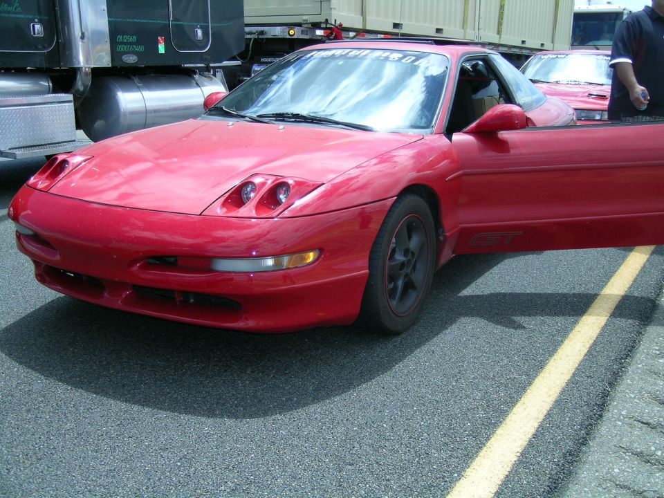 Red 1993 Ford Probe, driver's door open, parked next to a semi-truck